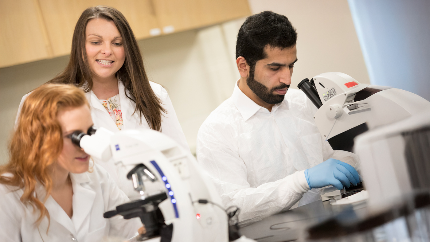 Professor and students in lab coats use microscopes