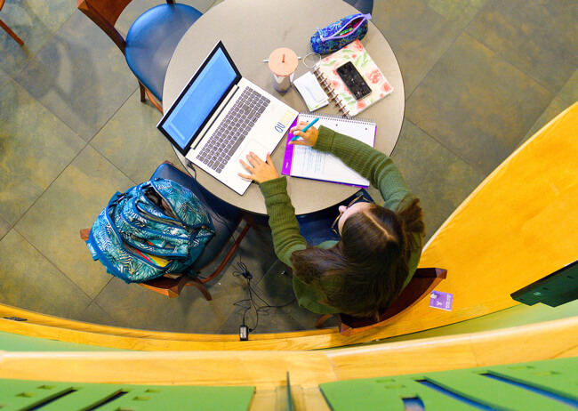 Aerial view of a student working at a table with a laptop and notebook in the Student Center Piazza