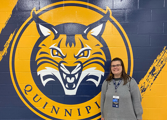 Madison Tornberg '27 standing in front of the Quinnipiac Logo