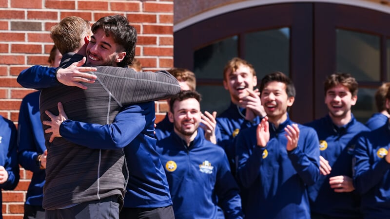 Rand Pecknold hugs a player while the men's ice hockey team cheers and claps