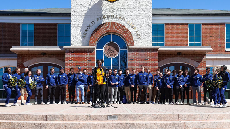 SGA president Owenea Roberts speaks at the microphones with the men's ice hockey team behind her