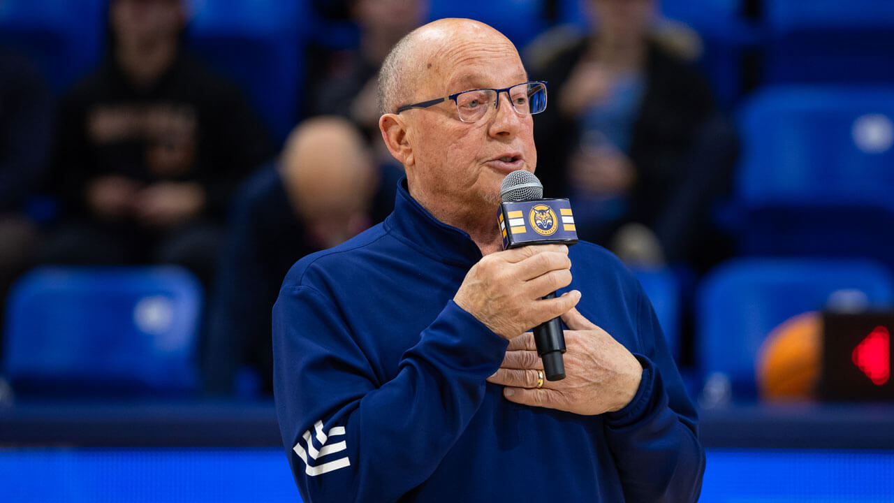 Man holds a Quinnipiac branded microphone while talking to the crowd at the M&T Bank Arena