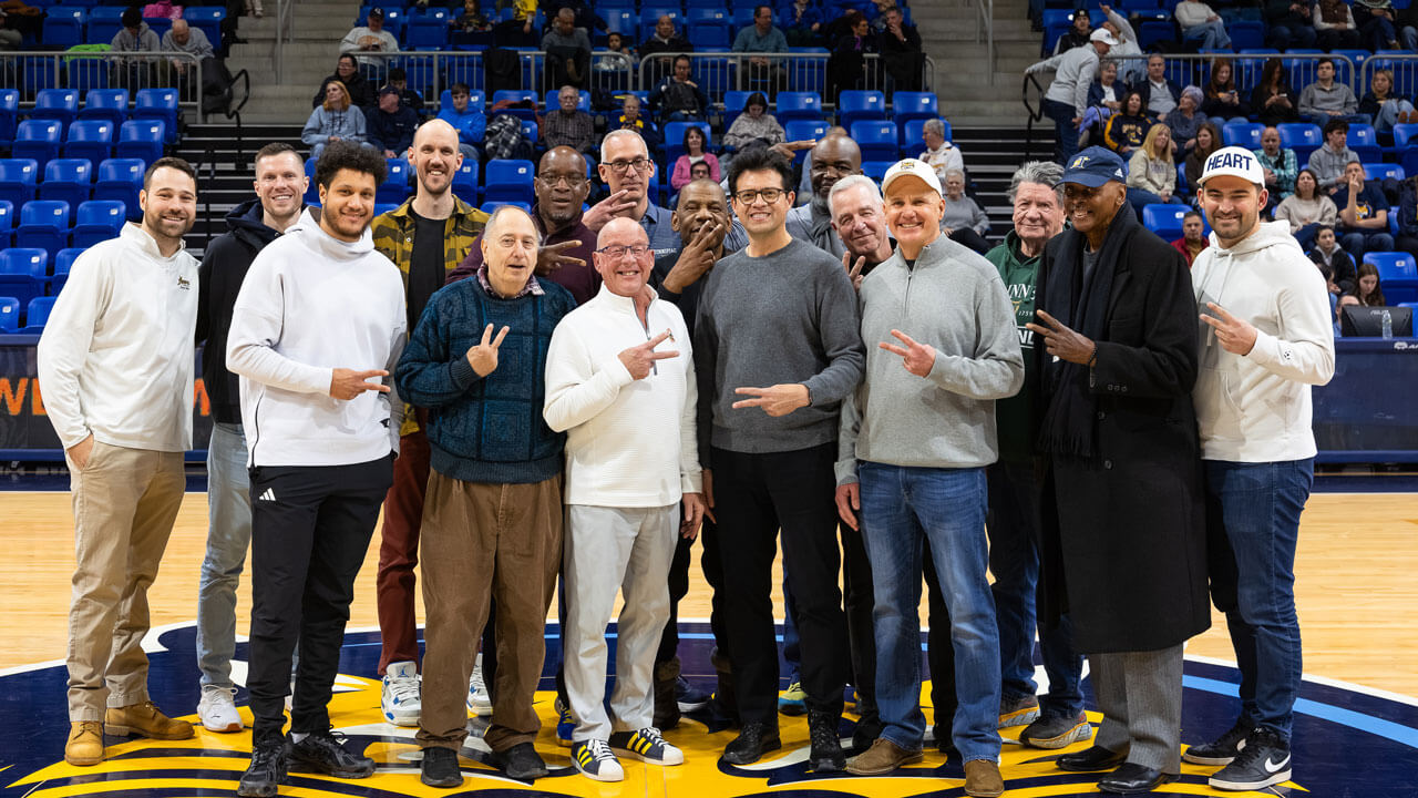 People smile in the middle of the court posing for a photo at M&T Bank Arena