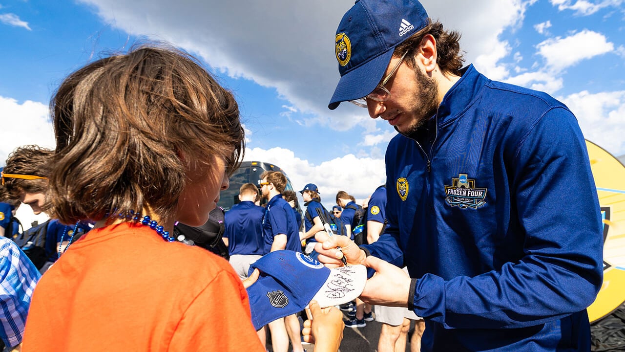 A men's ice hockey signs a young fan's hat.