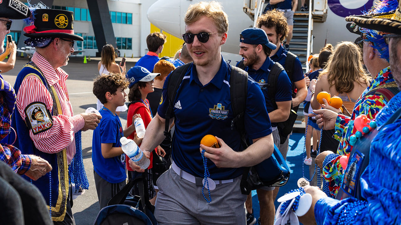 A member of the men's ice hockey team walks through a crowd.