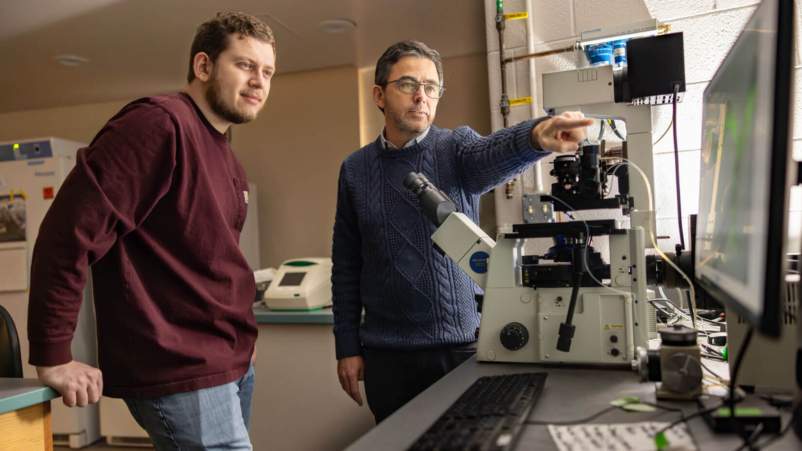 A biology professor directs a student during an experiment with microscopes..