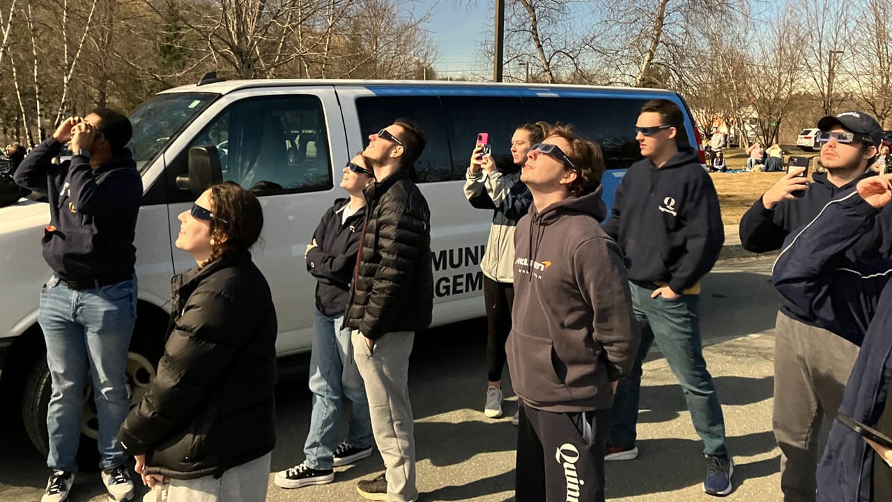 Students look up at the sky wearing solar eclipse glasses.