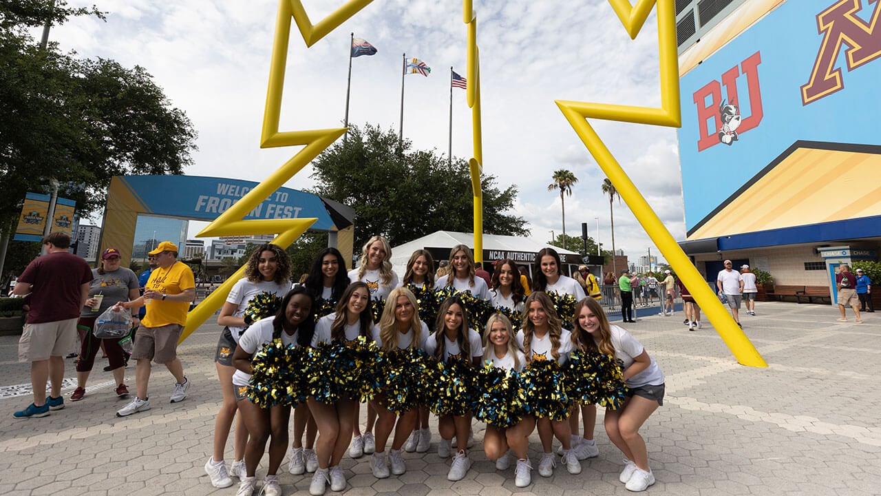 ice cats pose with pom poms underneath the Tampa lightning statue