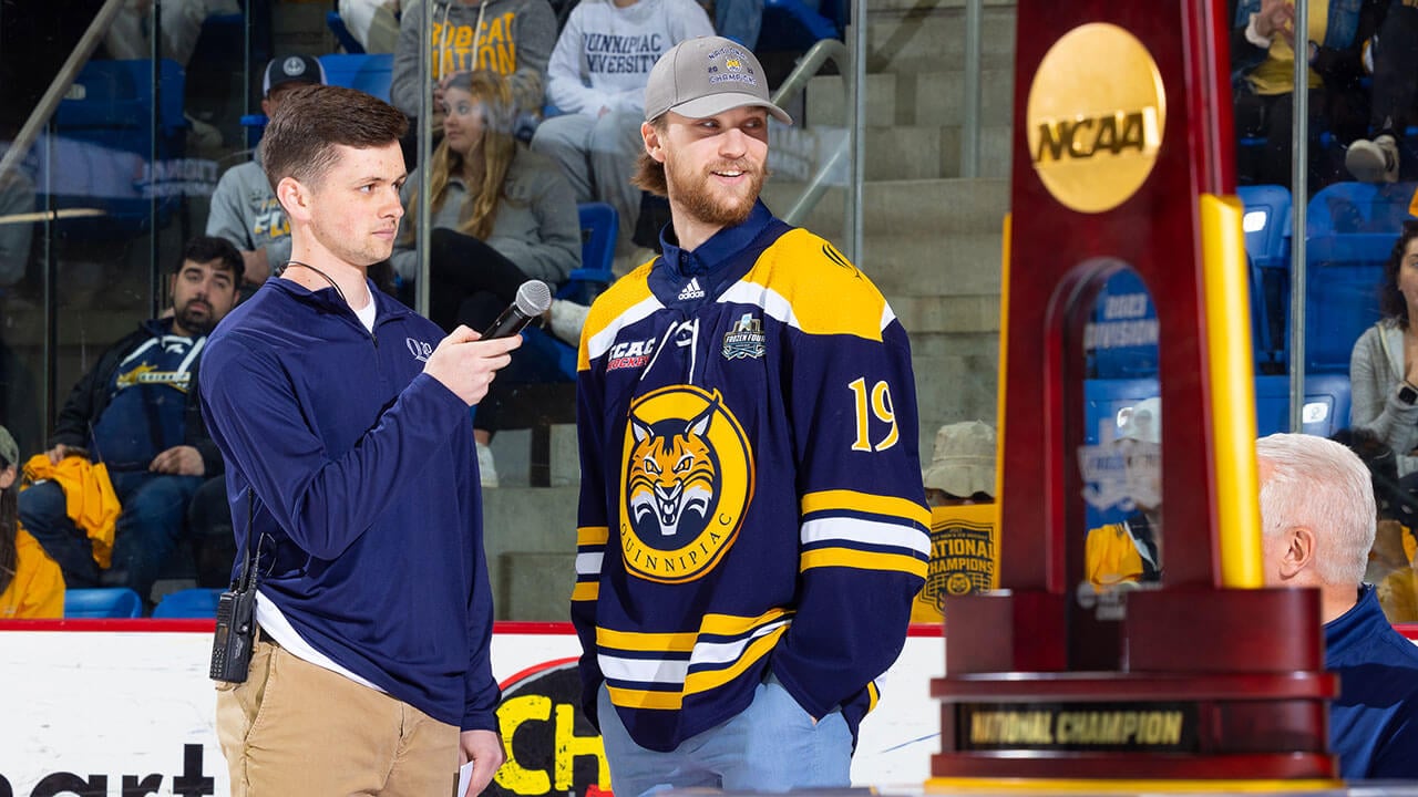 Quinnipiac hockey player TJ Friedmann smiles as he looks at the NCAA National Championship trophy