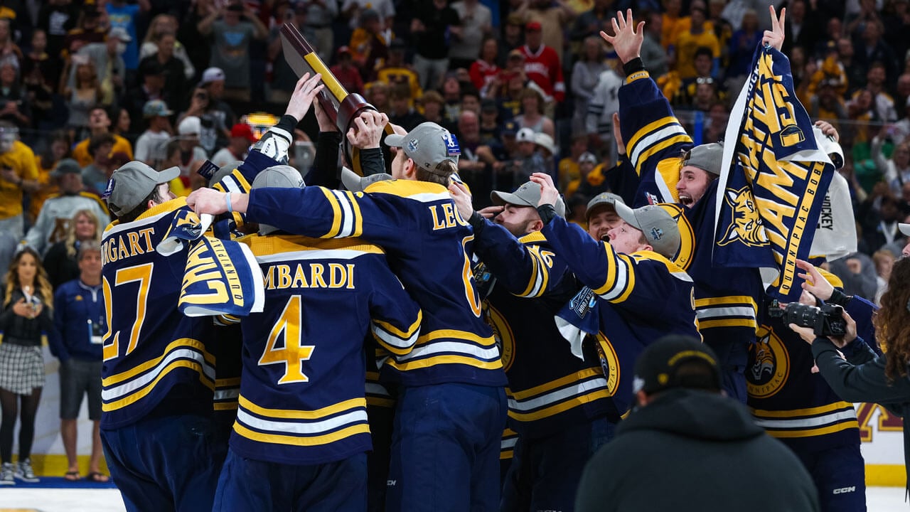 Quinnipiac ice hockey team crowding together to hold trophy