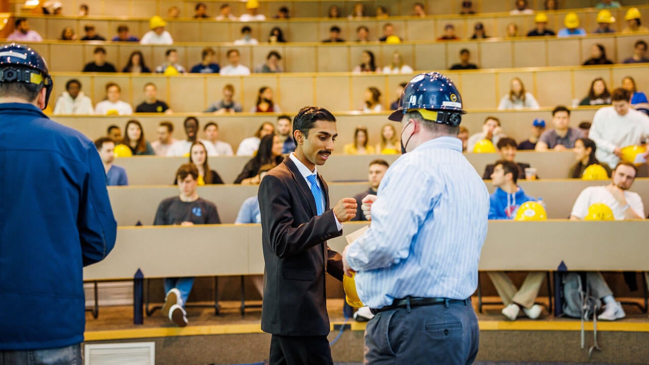 Student fist bumps professor at hard hat ceremony