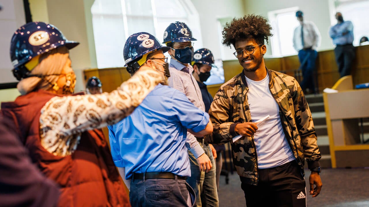 Student walking past professors while receiving award at hard hat ceremony