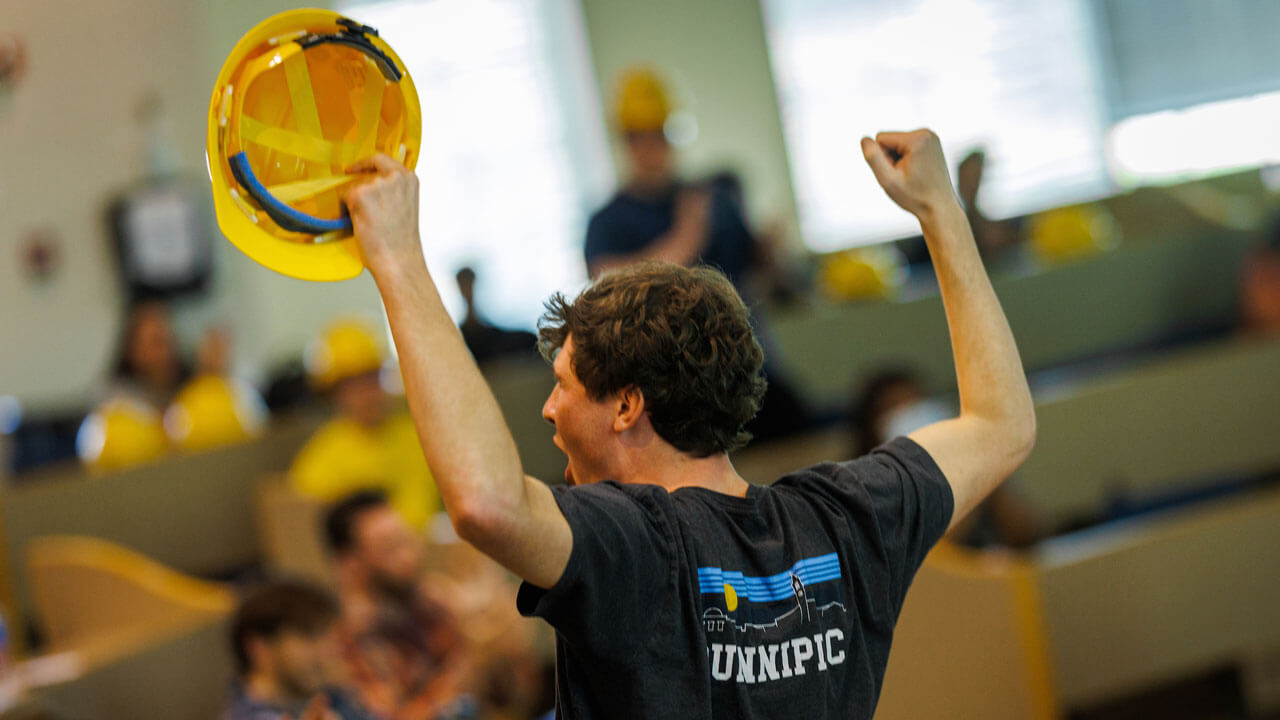 Student shouts in victory with hands and hard hat in the air