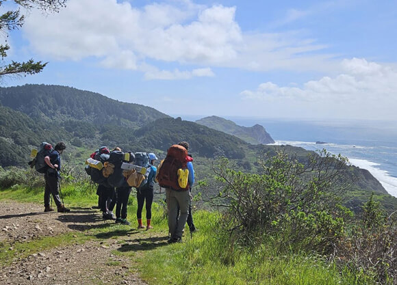 Students look out at a view of the ocean at the summit of a hike