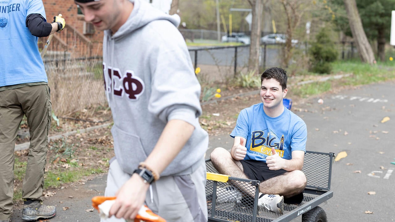 male student rides in a wagon pulled by another male student