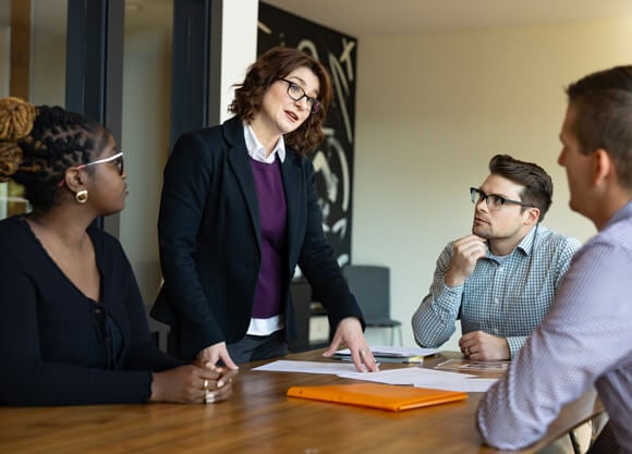 Graduate students and professionals collaborate and talk around a table in an office