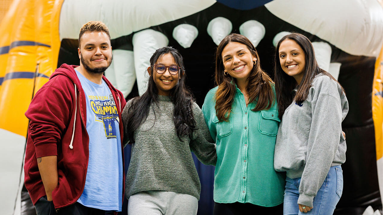 group of four students, one male and three female, pose in front of an inflatable bobcat smiling