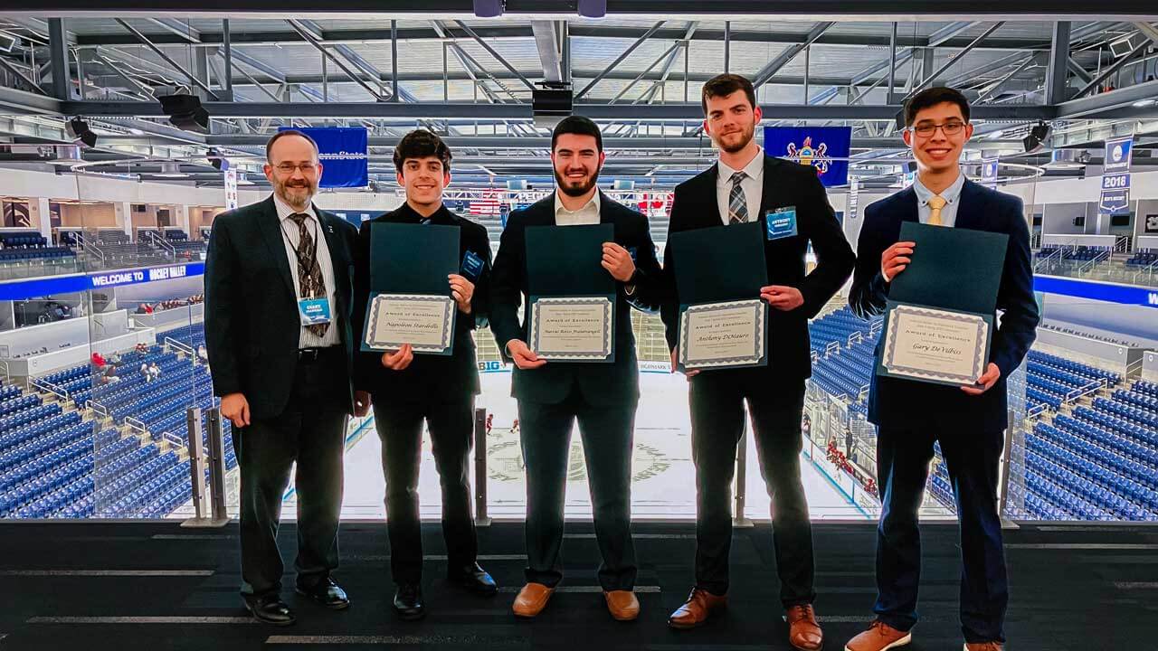 A professor and 4 male students posing for a photo with paper award certificates