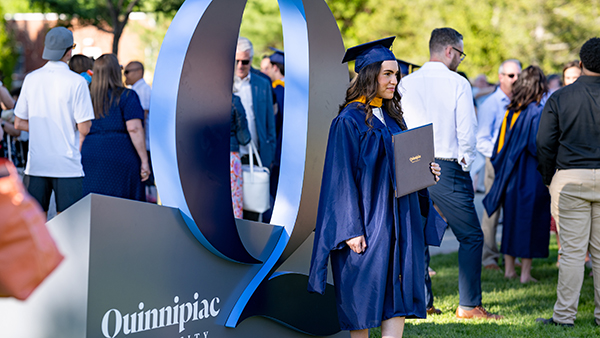 Student taking photos in their cap and gown in front of the Q statue
