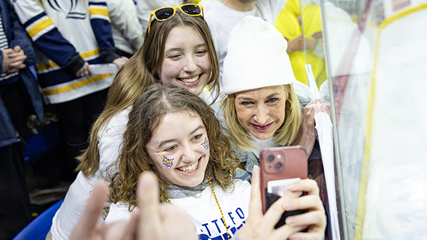 Students taking a selfie with President Marie Hardin at Men's Ice Hockey Yale Game