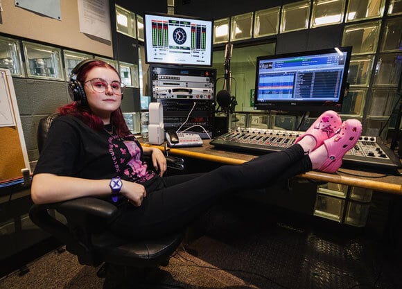 Jen Moglia sitting with legs resting on desk at WQAQ studio