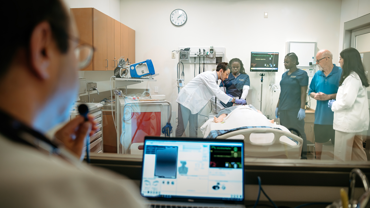 A professor observes students navigating a medical procedure in the simulation lab.