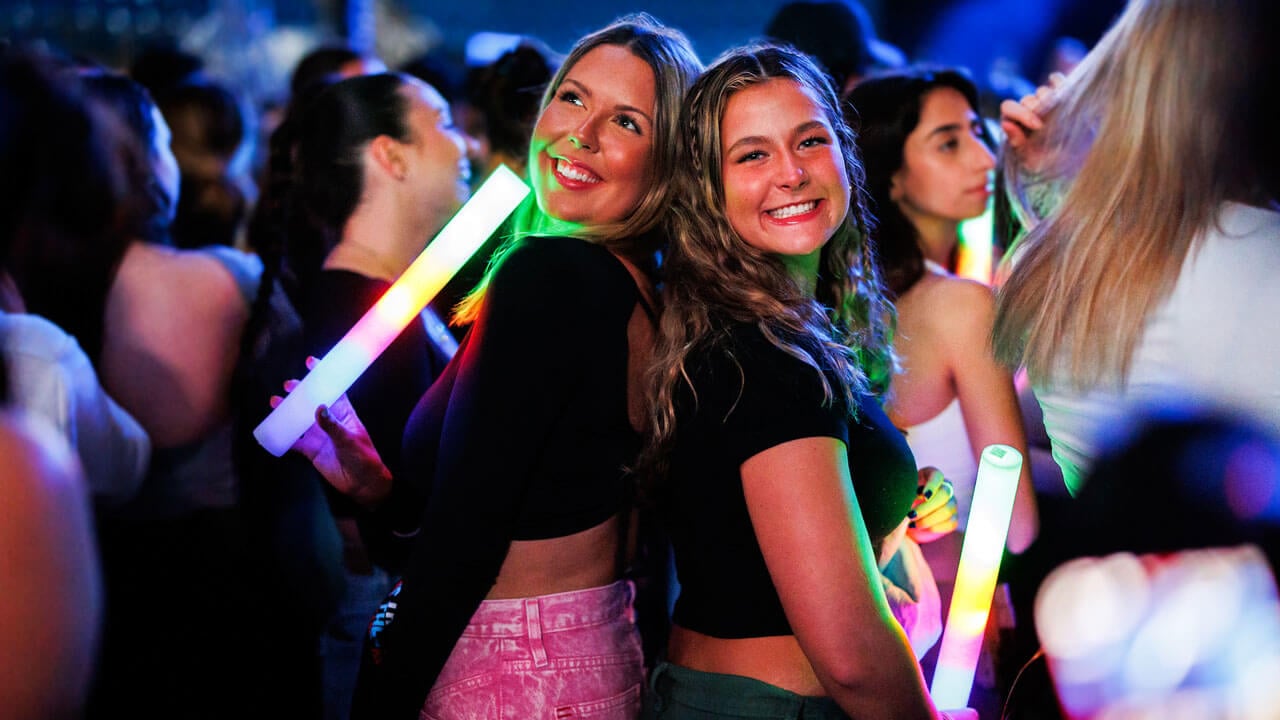 Two girls pose with their backs toward each other and smile in the crowd during Wake the Giant and Offset's performance