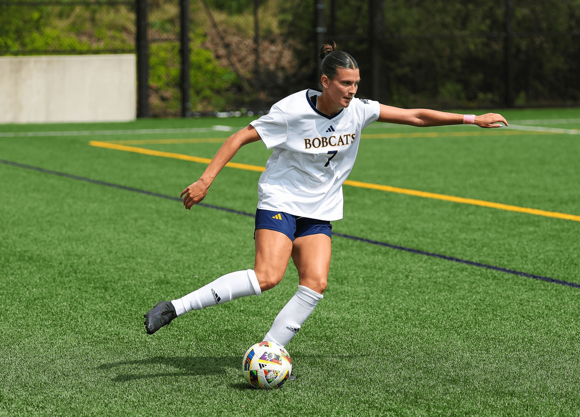 Natalie Lyon kicking a soccer ball on a turf field.