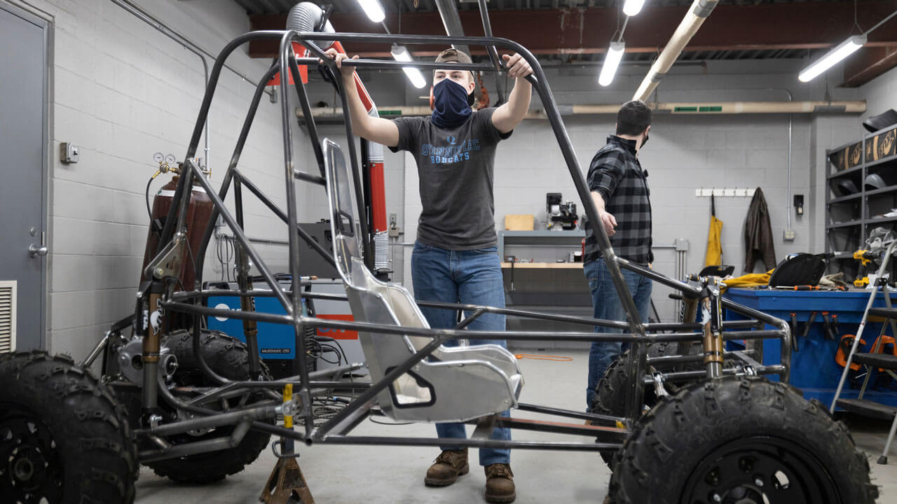 A student standing behind the frame of a vehicle.