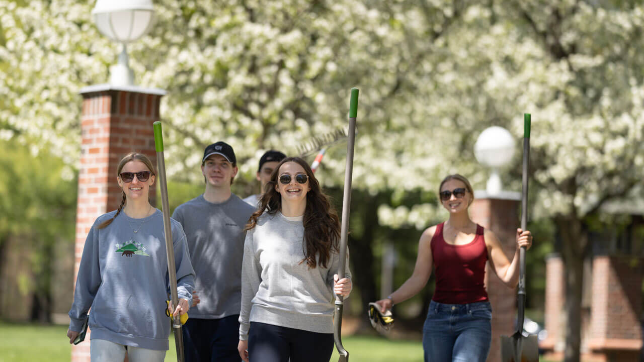 A group of students walk with gardening tools in hand