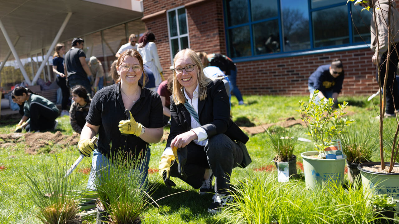 Professor and her student smile as they garden outside