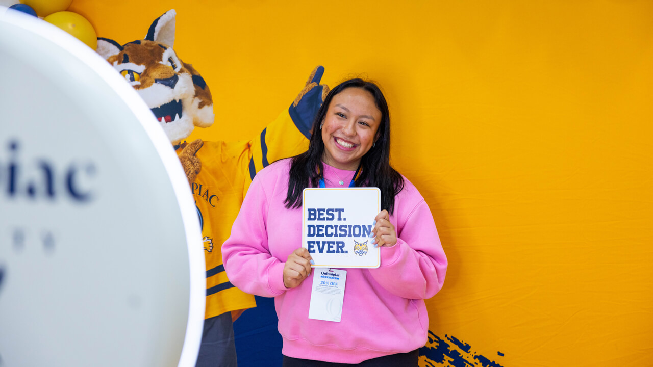 A newly admitted student smiles for a photo holding a sign that says "Best Decision Ever"