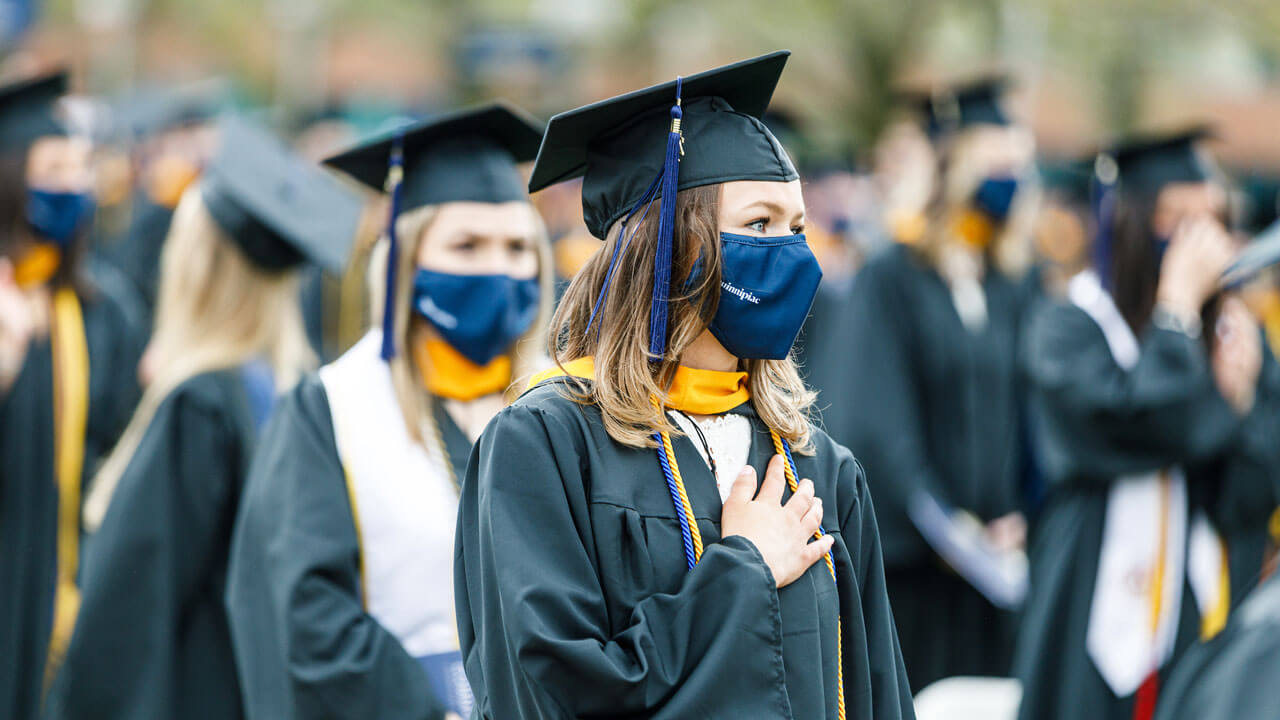 Graduates hold their hands on their hearts during the national anthem