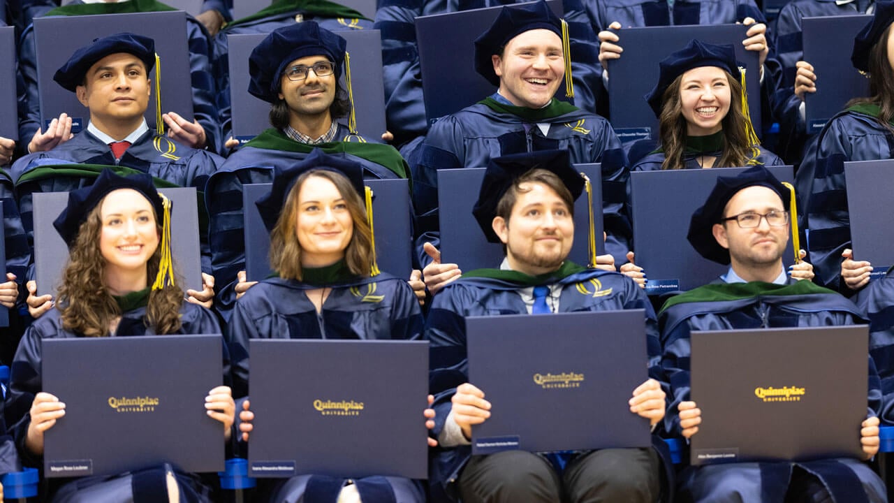 Graduates smiling while holding up their diplomas