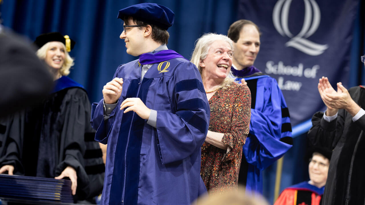 Student smiles as they receive their hood from their loved one.