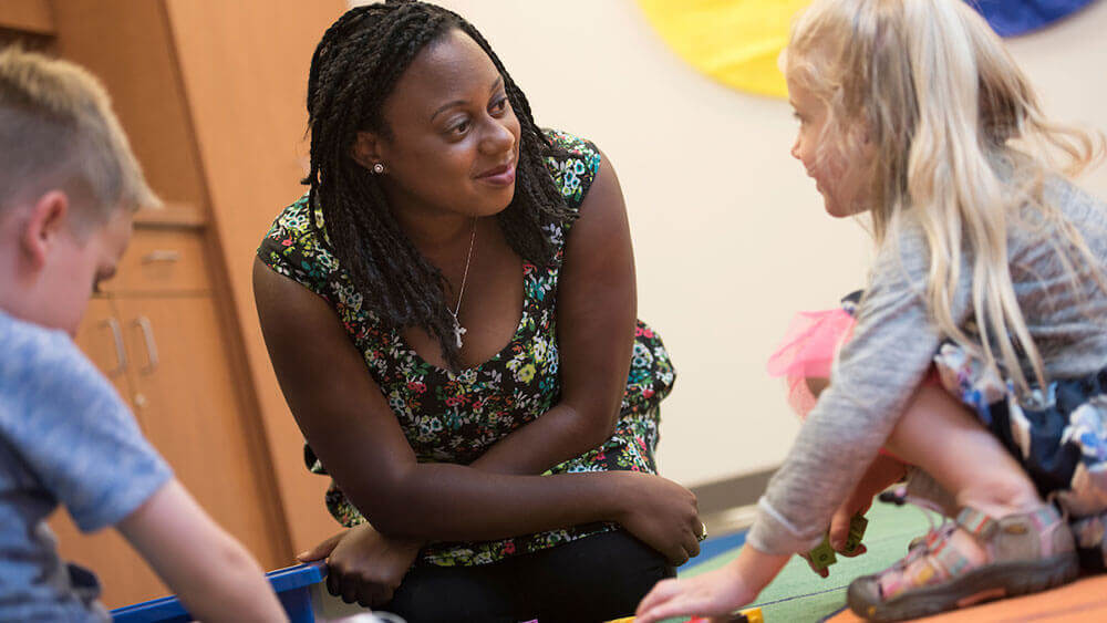 Education student Kyanna Joseph works with two first-grade students in a classroom.