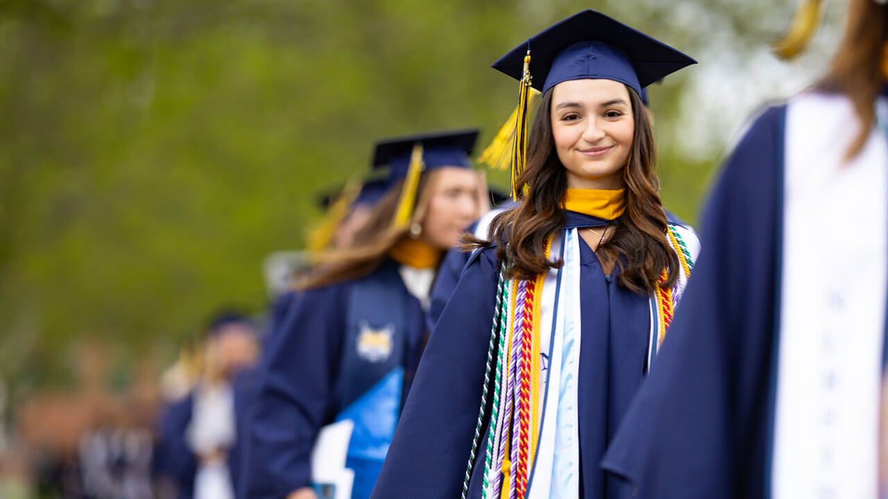 Student smiles as they process into commencement.