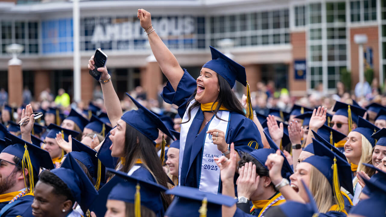 a female graduating student standing up and cheering in the crowd