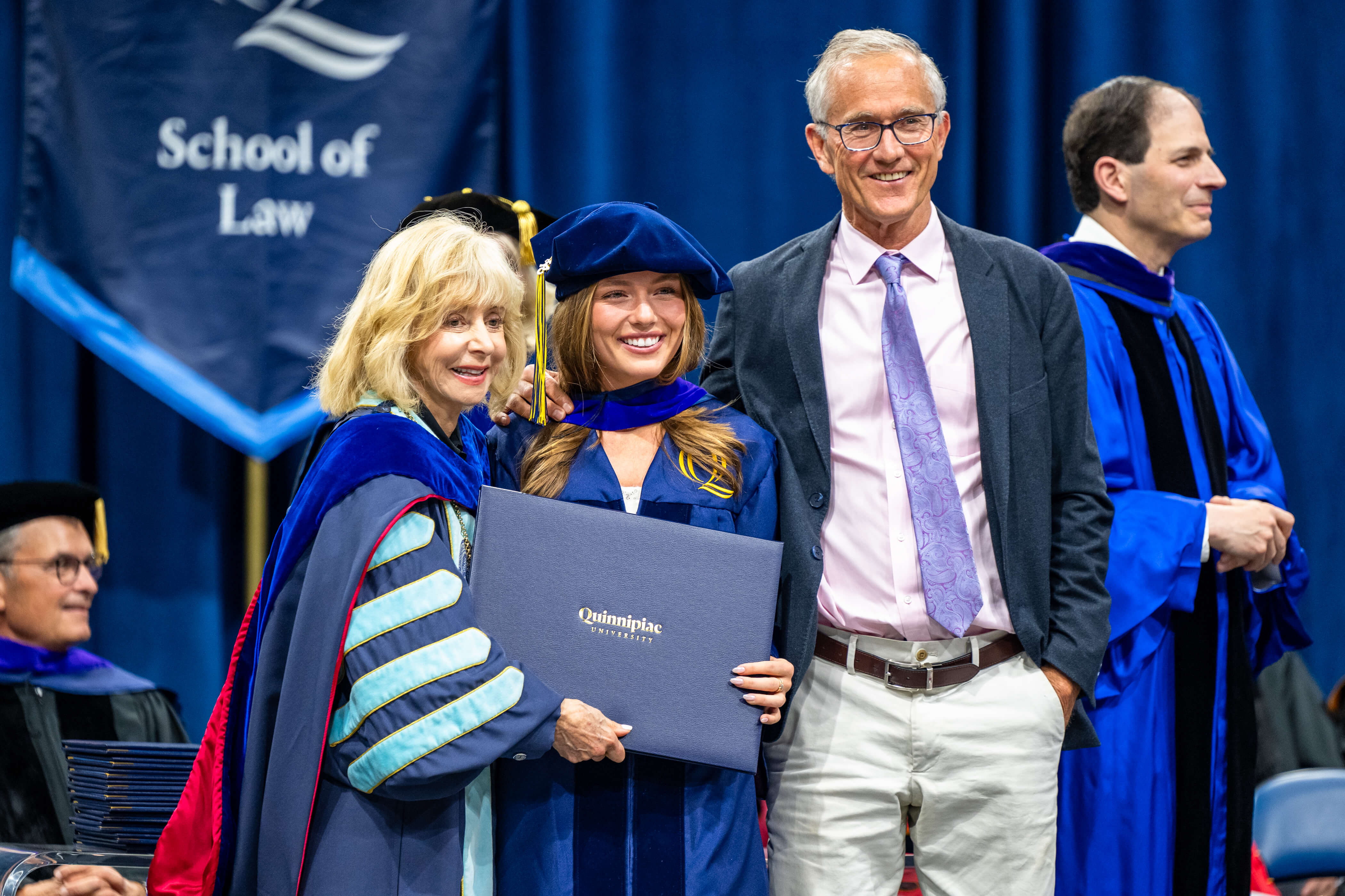 A graduate and their family member smiling on stage with President Judy Olian