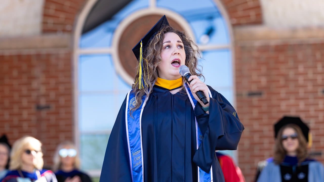 A graduate holds a microphone as she sings on stage