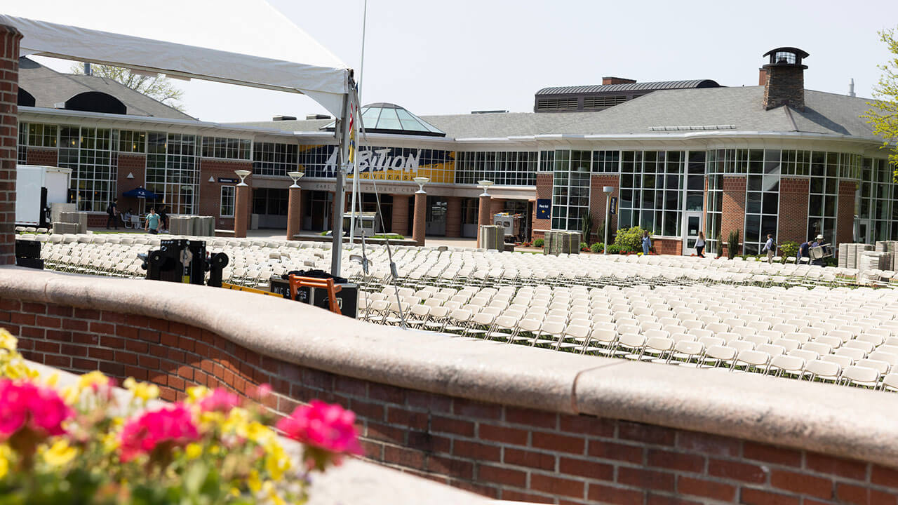 picture of rows of white graduation chairs with red flowers in the forefront and the student center behind them