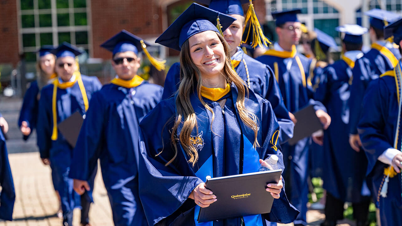 A student athlete holding their diploma and smiling