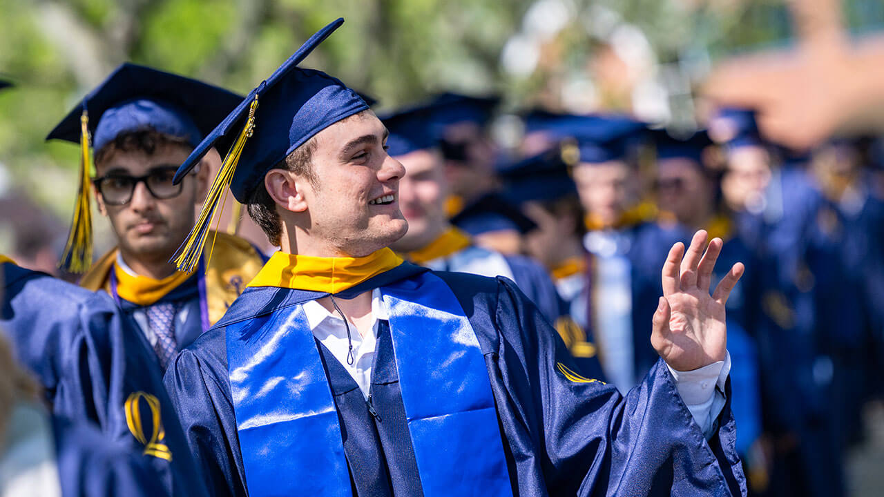 A graduate in the procession line waves into the distance