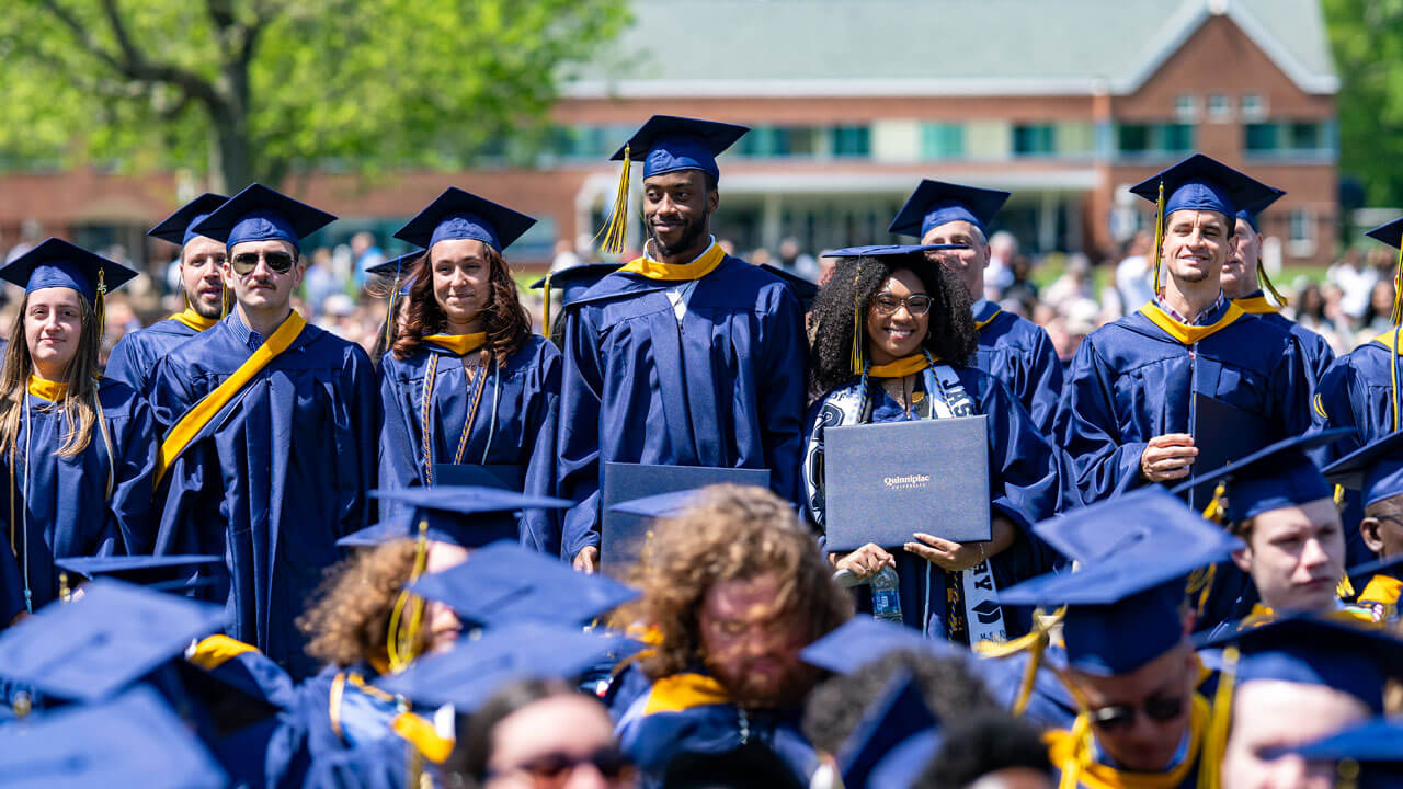 Graduates stand in the crowd with their diplomas.