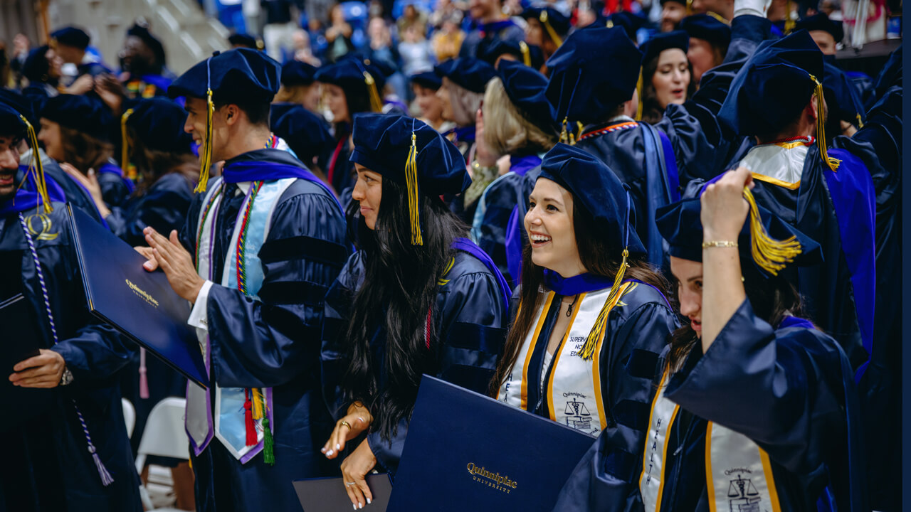 Dozens of graduates clap and smile as they stand by their seats