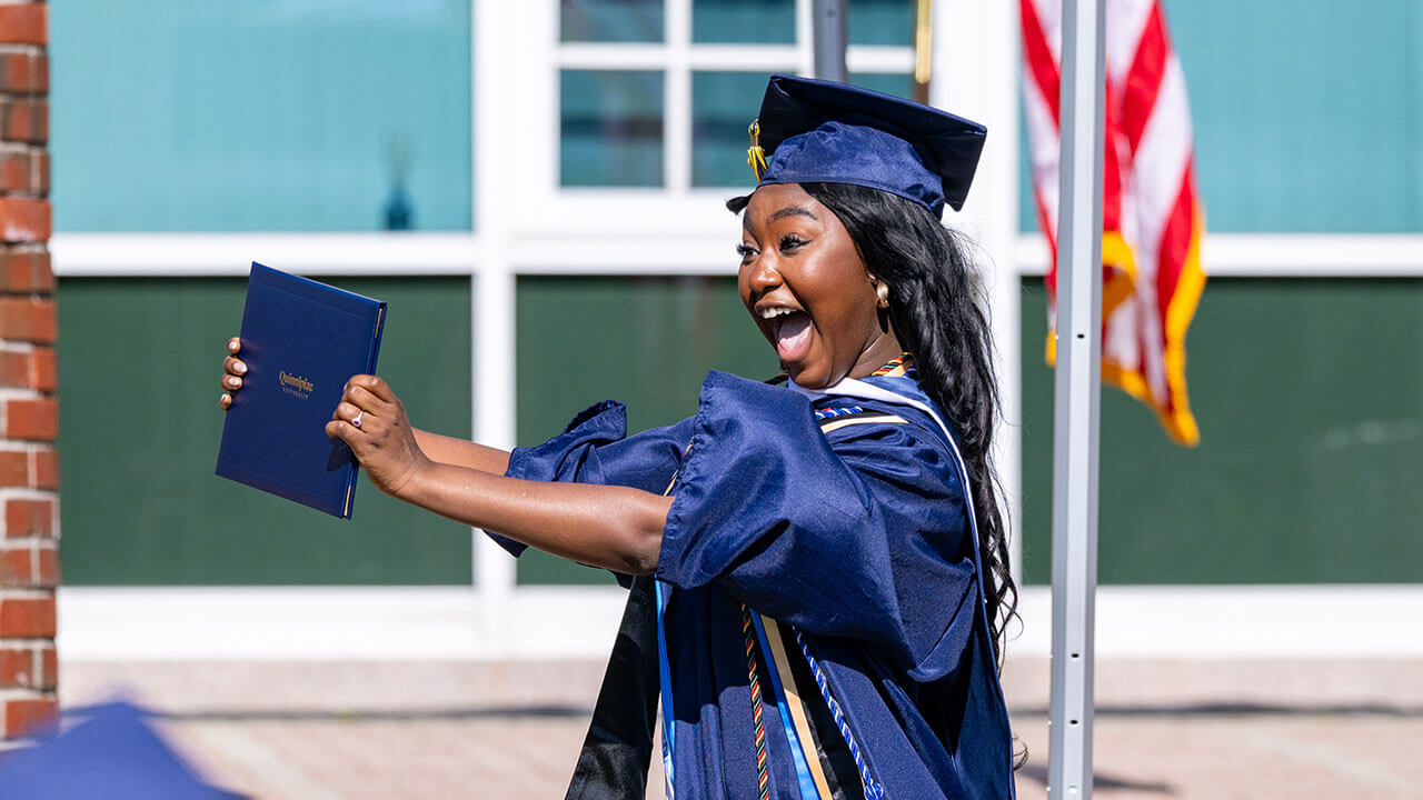 A graduate holds their diploma up excitedly