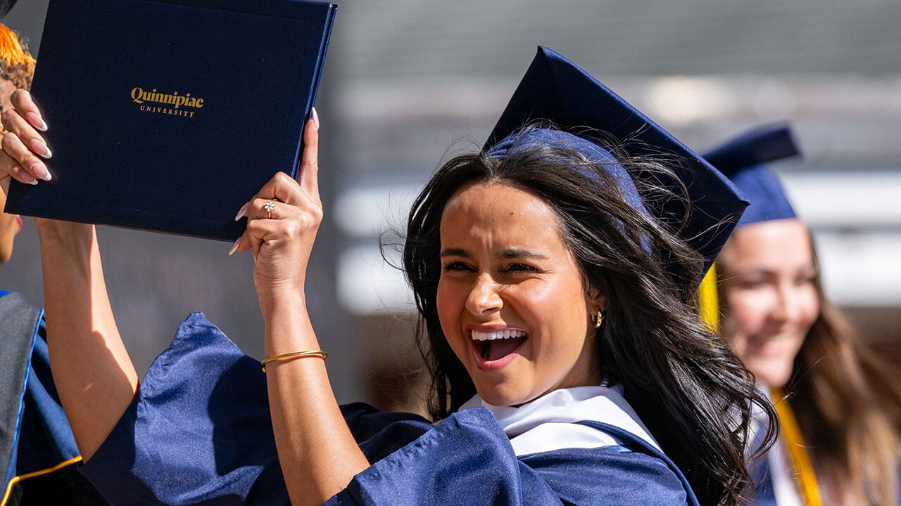 A graduate walks off stage excitedly holding up her diploma