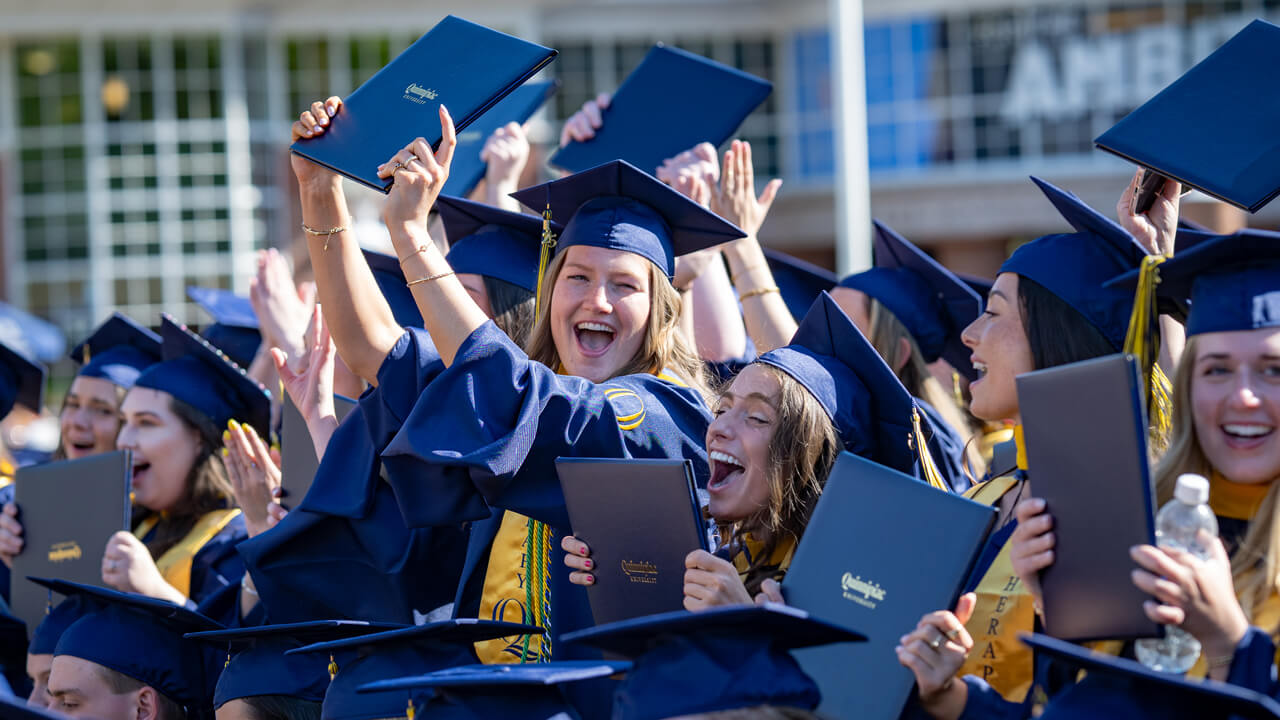 Grads in the crowd hold up their diplomas in excitement