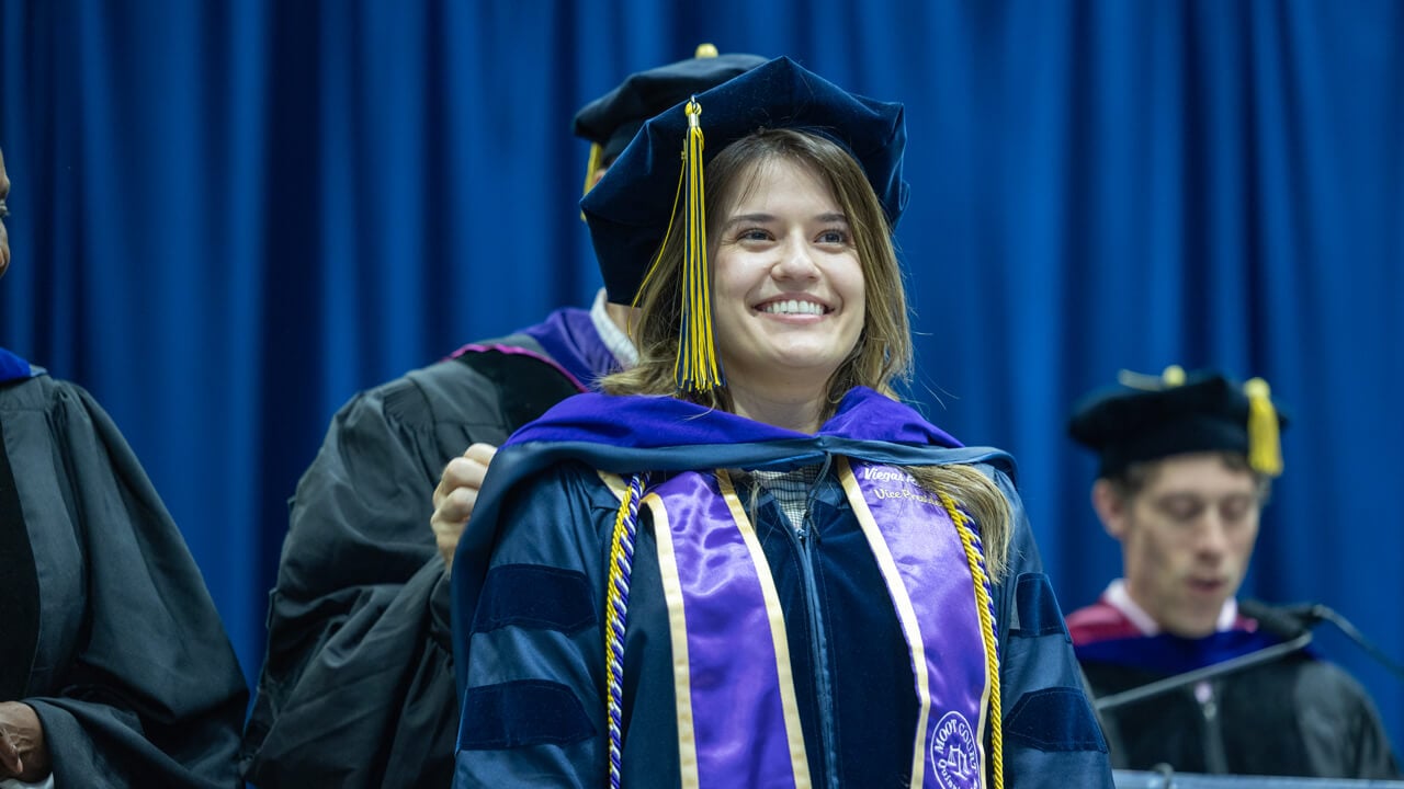 A graduate smiles proudly as a professor fluffs her doctoral hood