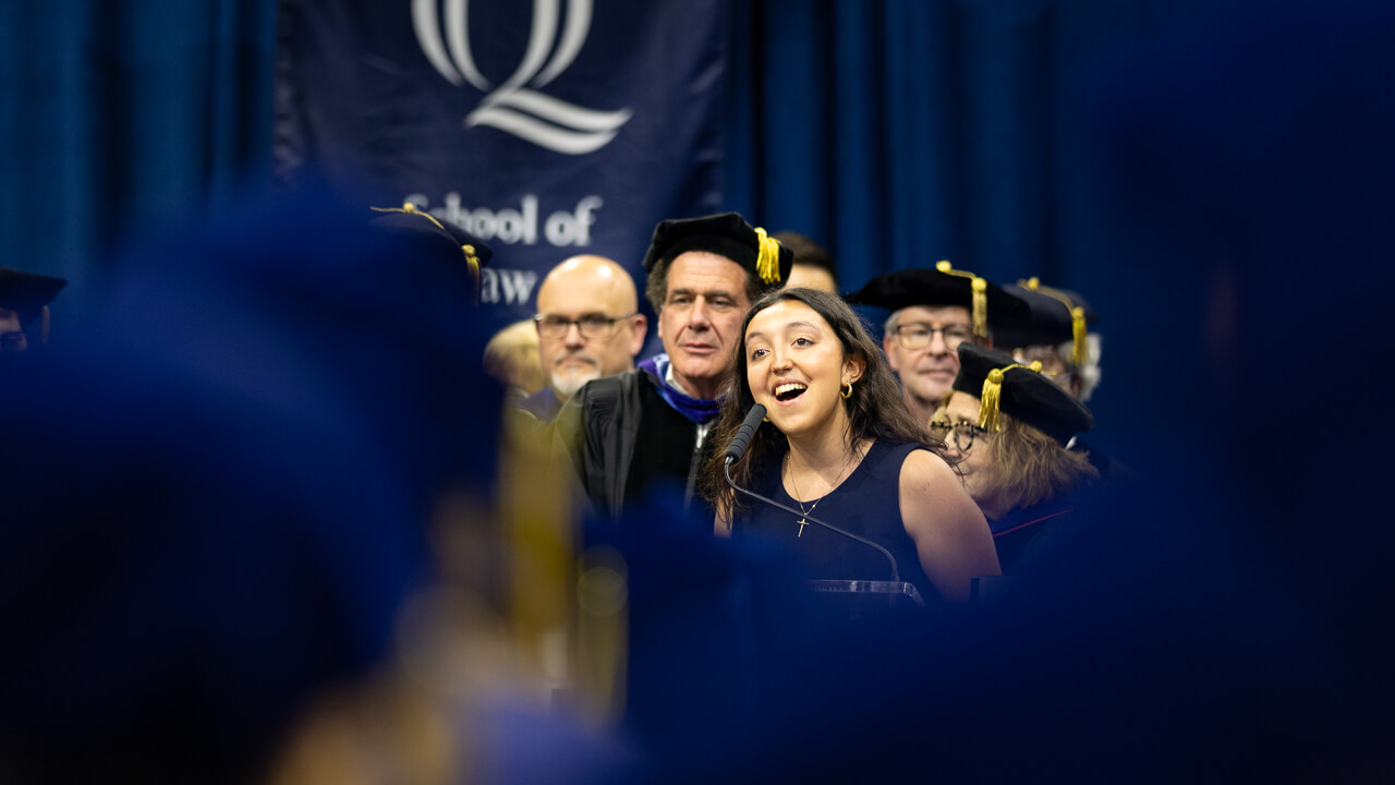 Kassidy Planas sings at a microphone at a podium among a crowd of people